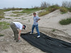SundownIsland > Jim Schuelke and Barbara Van Horn of Devon start with step one of the planting of new trees by laying out the tarp that will help protect them from overwhelming weeds. (photo by Peggy Wilkinson)