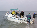 SundownIsland > The first crew arrives.  It was a windy choppy trip, typical for a March workday. Tim Wilkinson and his brother, Doug, help unload the boat while Diane Nunley, Marcy Spearsl, Ethan Vuichard and Abe Moore passed over supplies and equipment. Richard Prater (on bow) and Ed Taylor (yellow slicker) secure the Egret II. (Photo credit: Rebeka Olson)